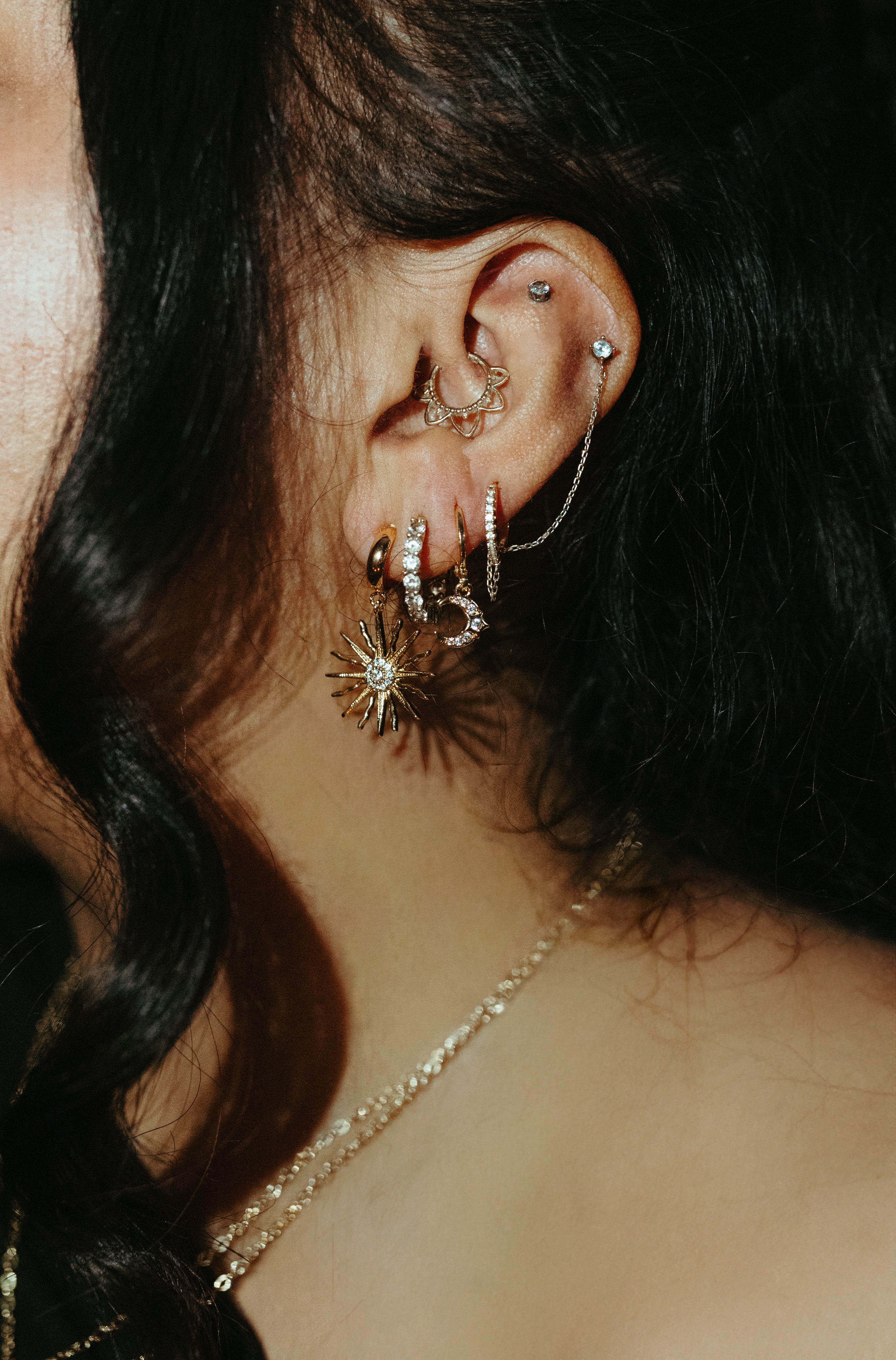 Woman wearing gold huggie earrings with circular drop in layered ear stack