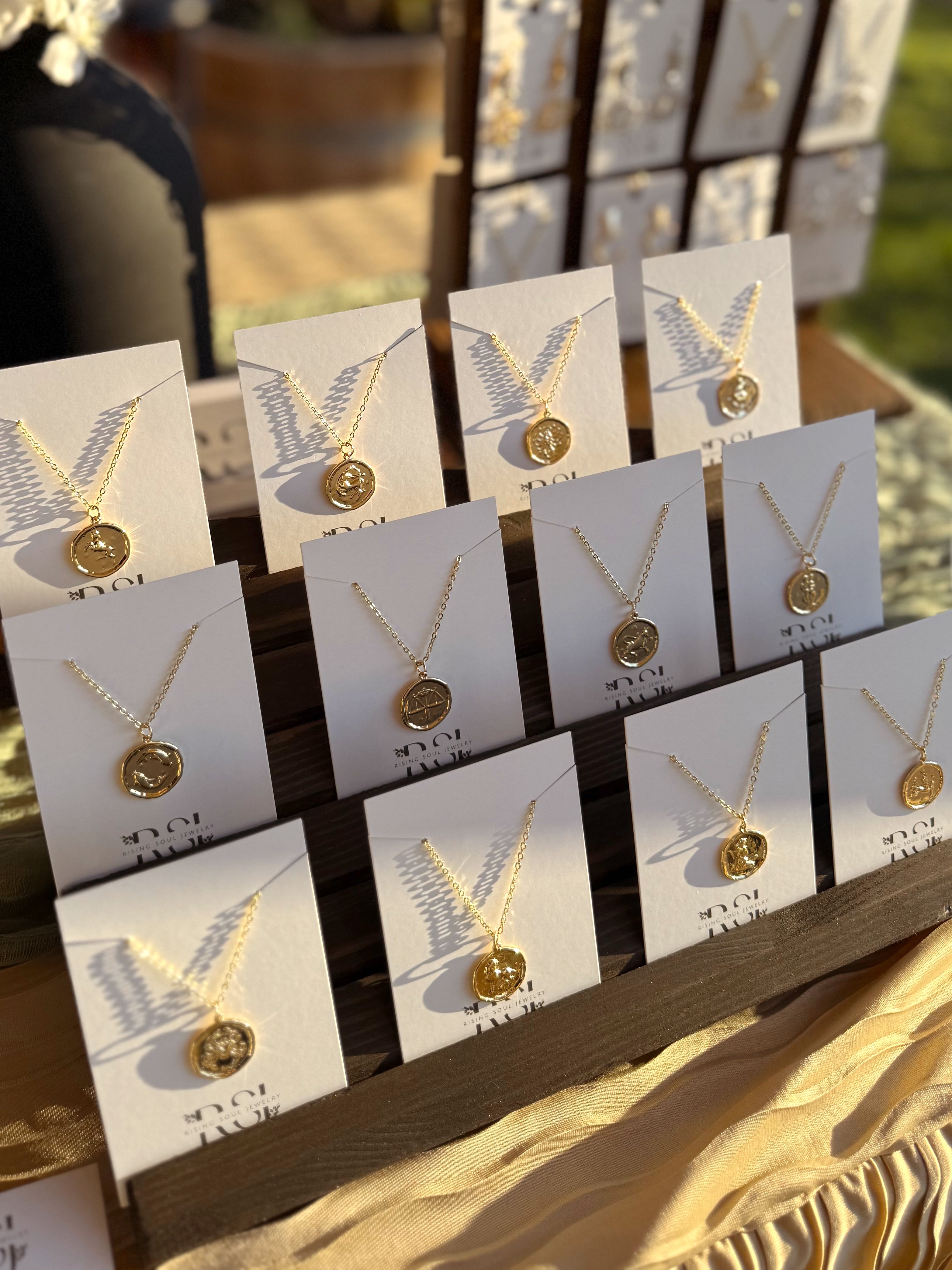 Gold zodiac coin necklaces displayed on cards, jewelry collection setup
